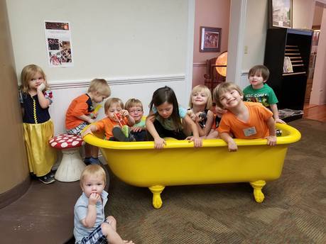 Photo of preschool children setting in yellow reading tub that is filled stuffed animals.